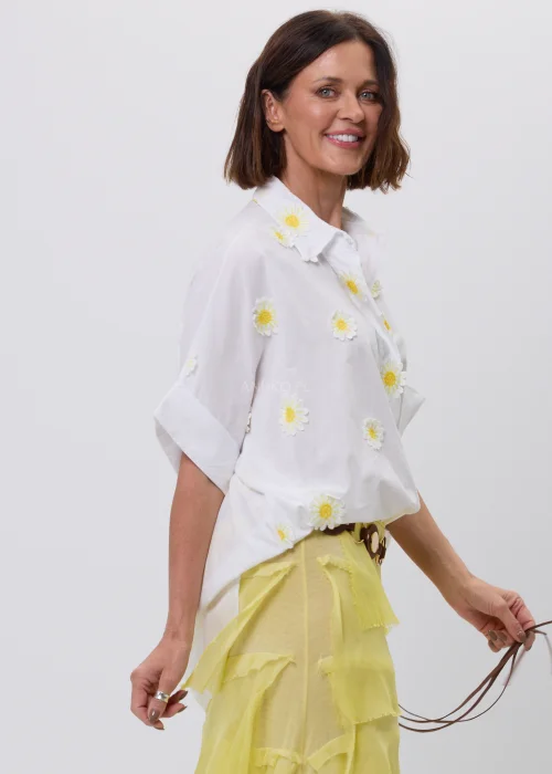Biała koszula damska z dekoracyjnymi aplikacjami w kształcie stokrotek, krótkim podwiniętym rękawem i klasycznym kołnierzykiem. Luźny model w stylu boho, idealny do letnich stylizacji ze spódnicami i lekkimi spodniami.