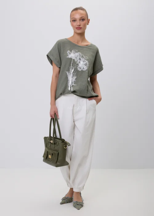 Oliwkowy damski T-shirt oversize z białym kwiatowym nadrukiem i podwijanymi rękawami. Luźna bluzka w naturalnym stylu, zestawiona z białymi szerokimi spodniami i torebką, idealna do codziennych stylizacji.