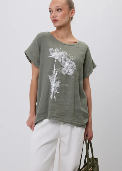Oliwkowy damski T-shirt oversize z białym kwiatowym nadrukiem i podwijanymi rękawami. Luźna bluzka w naturalnym stylu, zestawiona z białymi szerokimi spodniami i torebką, idealna do codziennych stylizacji.