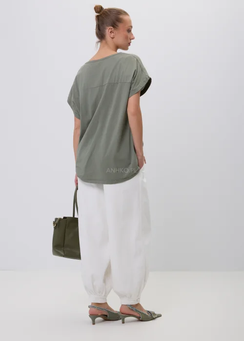 Oliwkowy damski T-shirt oversize z białym kwiatowym nadrukiem i podwijanymi rękawami. Luźna bluzka w naturalnym stylu, zestawiona z białymi szerokimi spodniami i torebką, idealna do codziennych stylizacji.