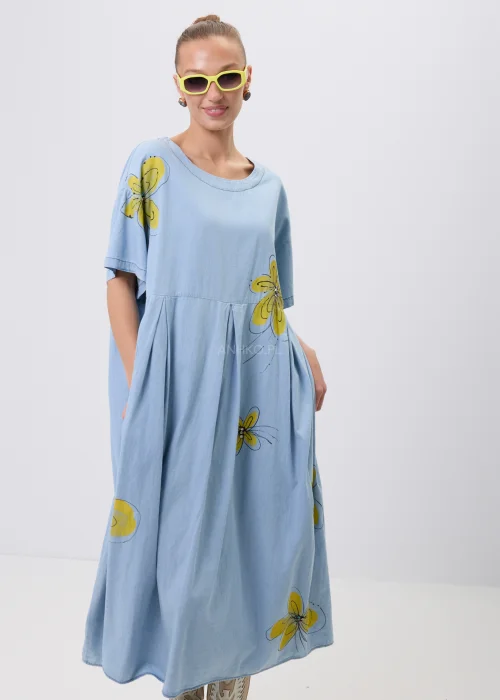 Błękitna sukienka maxi oversize z krótkim rękawem i efektownym nadrukiem dużych żółtych kwiatów. Luźny fason z odcięciem pod biustem zapewnia swobodę noszenia i tworzy lekką, kobiecą stylizację na co dzień.