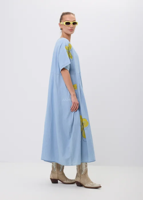 Błękitna sukienka maxi oversize z krótkim rękawem i efektownym nadrukiem dużych żółtych kwiatów. Luźny fason z odcięciem pod biustem zapewnia swobodę noszenia i tworzy lekką, kobiecą stylizację na co dzień.