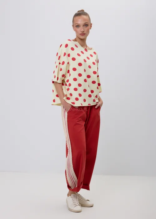 Kremowa damska bluzka oversize w czerwone grochy z rękawem 3/4, zestawiona z czerwonymi spodniami z koronkowym lampasem. Modna stylizacja casual inspirowana stylem retro i francuską elegancją.