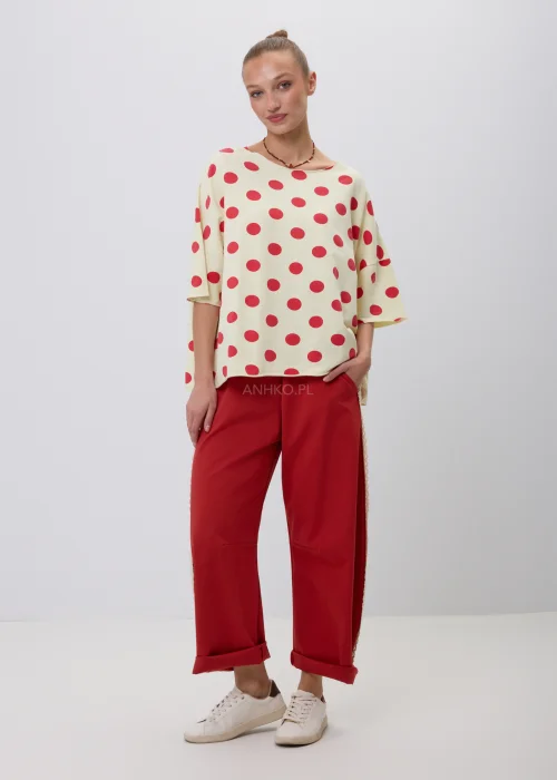 Kremowa damska bluzka oversize w czerwone grochy z rękawem 3/4, zestawiona z czerwonymi spodniami z koronkowym lampasem. Modna stylizacja casual inspirowana stylem retro i francuską elegancją.