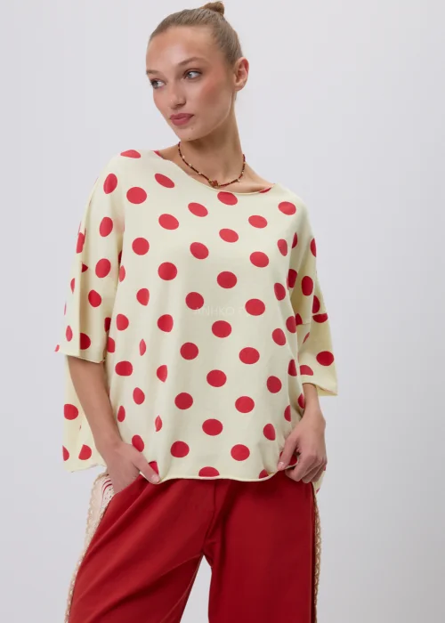 Kremowa damska bluzka oversize w czerwone grochy z rękawem 3/4, zestawiona z czerwonymi spodniami z koronkowym lampasem. Modna stylizacja casual inspirowana stylem retro i francuską elegancją.