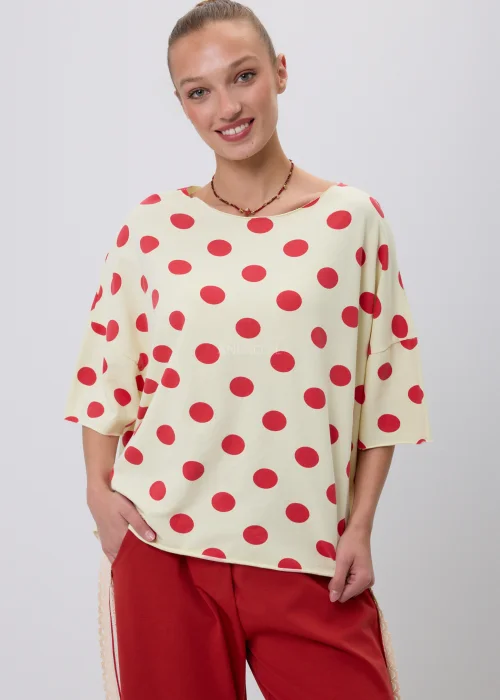Kremowa damska bluzka oversize w czerwone grochy z rękawem 3/4, zestawiona z czerwonymi spodniami z koronkowym lampasem. Modna stylizacja casual inspirowana stylem retro i francuską elegancją.