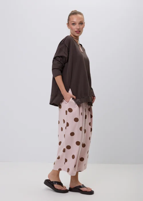 Brązowa bluza damska oversize z długim rękawem i okrągłym dekoltem, o swobodnym fasonie z ozdobnymi przeszyciami. Casualowa stylizacja z szerokimi spodniami w grochy podkreśla wygodny i nowoczesny charakter modelu.