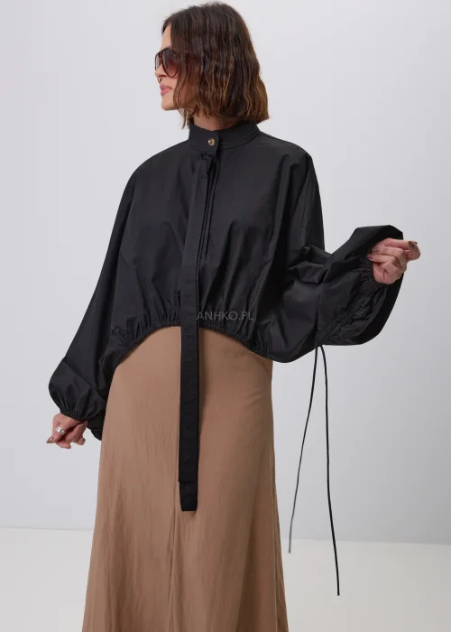 Czarna damska kurtka bomber oversize ze stójką, szerokimi rękawami i regulowanymi troczkami przy mankietach. Nowoczeska stylizacja casual z krótką kurtką i beżową spódnicą maxi.