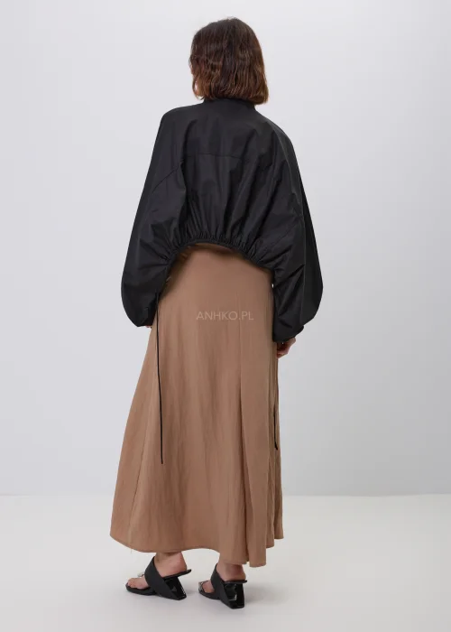 Czarna damska kurtka bomber oversize ze stójką, szerokimi rękawami i regulowanymi troczkami przy mankietach. Nowoczeska stylizacja casual z krótką kurtką i beżową spódnicą maxi.