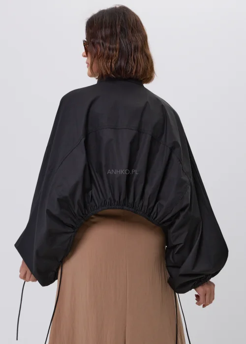 Czarna damska kurtka bomber oversize ze stójką, szerokimi rękawami i regulowanymi troczkami przy mankietach. Nowoczeska stylizacja casual z krótką kurtką i beżową spódnicą maxi.