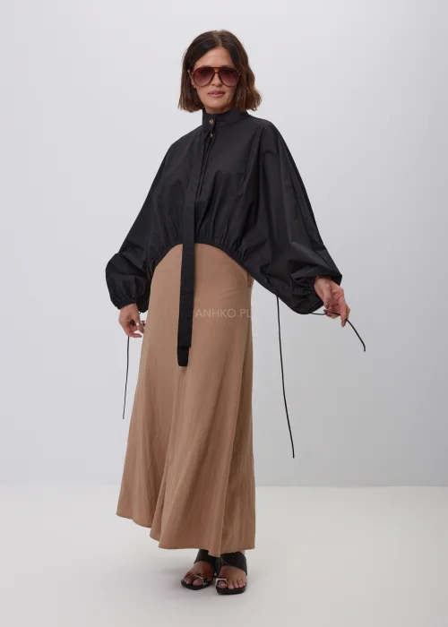 Czarna damska kurtka bomber oversize ze stójką, szerokimi rękawami i regulowanymi troczkami przy mankietach. Nowoczeska stylizacja casual z krótką kurtką i beżową spódnicą maxi.