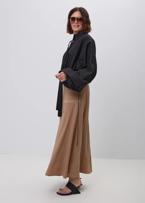 Czarna damska kurtka bomber oversize ze stójką, szerokimi rękawami i regulowanymi troczkami przy mankietach. Nowoczeska stylizacja casual z krótką kurtką i beżową spódnicą maxi.