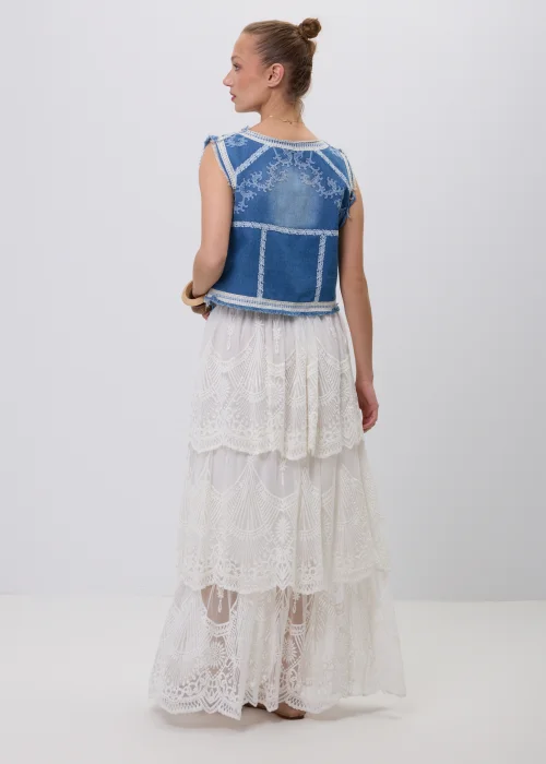 Biała koronkowa spódnica maxi w stylu boho z warstwowymi falbanami, ażurowymi haftami i ozdobnym brązowym paskiem w talii. Romantyczny model o efektownym wykończeniu, idealny do letnich i eleganckich stylizacji.