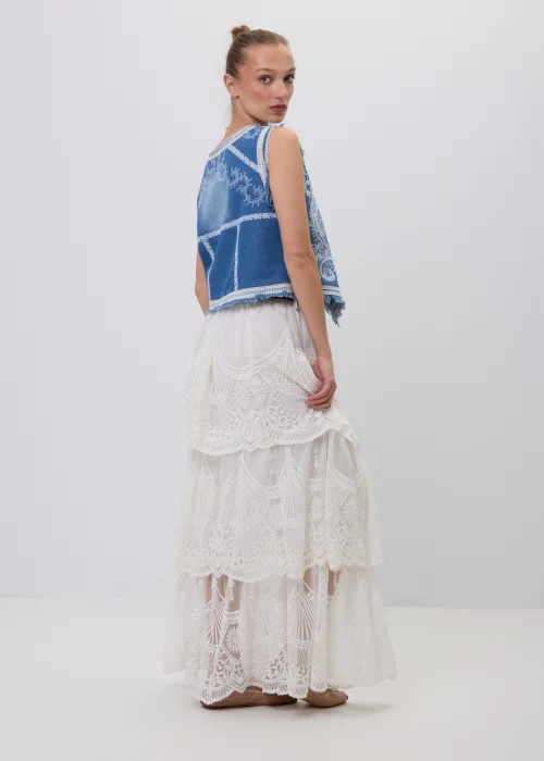 Biała koronkowa spódnica maxi w stylu boho z warstwowymi falbanami, ażurowymi haftami i ozdobnym brązowym paskiem w talii. Romantyczny model o efektownym wykończeniu, idealny do letnich i eleganckich stylizacji.