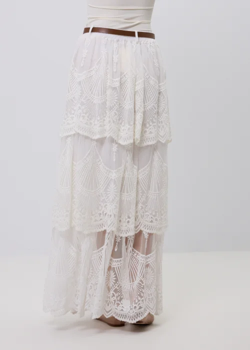 Biała koronkowa spódnica maxi w stylu boho z warstwowymi falbanami, ażurowymi haftami i ozdobnym brązowym paskiem w talii. Romantyczny model o efektownym wykończeniu, idealny do letnich i eleganckich stylizacji.