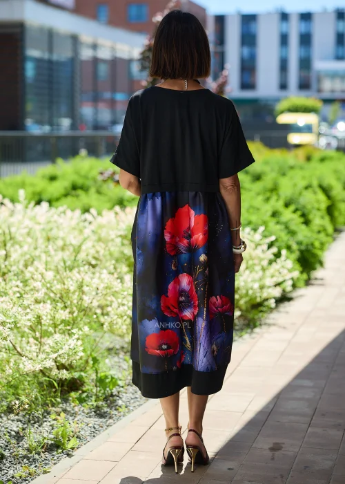 Czarna sukienka midi damska z efektownym nadrukiem czerwonych maków na granatowym tle, o luźnym fasonie i krótkich rękawach. Elegancka stylizacja z ozdobnym naszyjnikiem i bordowymi czółenkami.