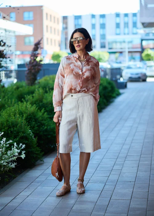Beżowe bermudy damskie z dodatkiem lnu, o długości do kolan i klasycznym fasonie z zapięciem na guzik, prezentowane w eleganckiej miejskiej stylizacji.