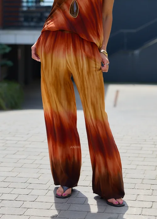 Zwiewne spodnie palazzo z efektem ombre w odcieniach karmelu, miedzi i ciemnego brązu. Szerokie nogawki oraz lekko kreszowana tkanina nadają modelowi elegancki, płynny wygląd idealny do stylizacji boho i resort.