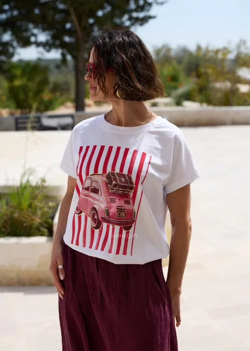 Biały damski T-shirt z czerwonym nadrukiem retro samochodu i pionowymi pasami, w zestawieniu z bordowymi spodniami o luźnym fasonie.