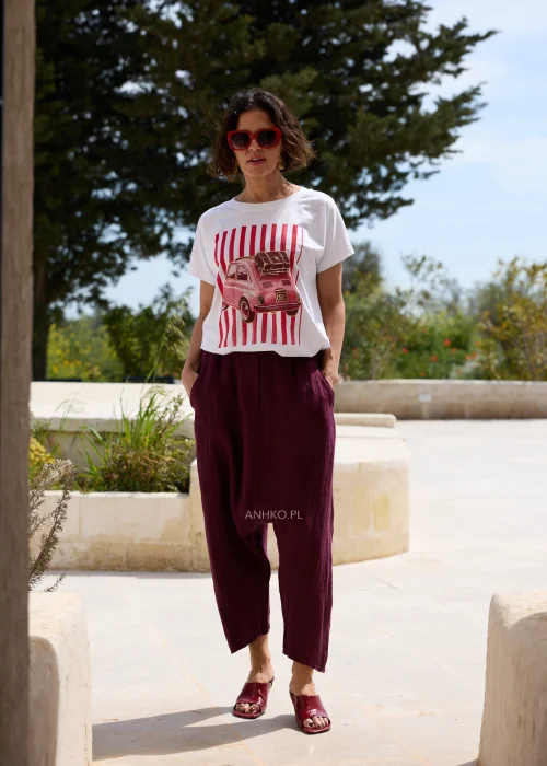 Biały damski T-shirt z czerwonym nadrukiem retro samochodu i pionowymi pasami, w zestawieniu z bordowymi spodniami o luźnym fasonie.