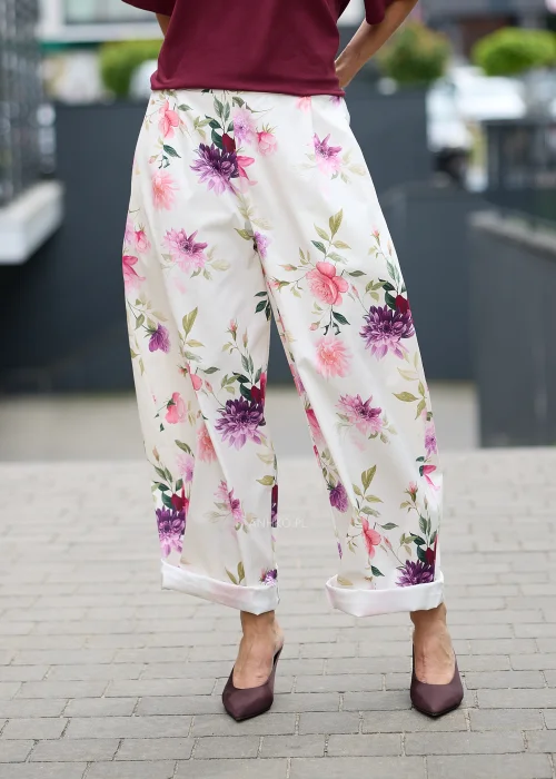 Kremowe spodnie w kwiatowy print z szeroką nogawką i elastyczną talią. Lekki model w różowo-fioletowe kwiaty idealny do romantycznych i kobiecych stylizacji.