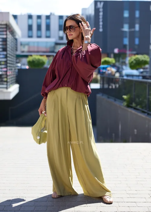 Bordowa koszula oversize z bufiastymi rękawami, zestawiona z oliwkowymi szerokimi spodniami i jasną kopertówką w eleganckiej stylizacji
