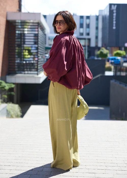 Bordowa koszula oversize z bufiastymi rękawami, zestawiona z oliwkowymi szerokimi spodniami i jasną kopertówką w eleganckiej stylizacji