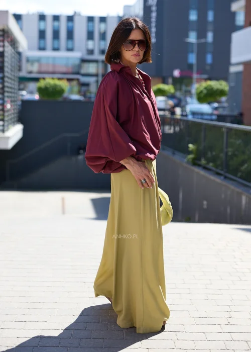 Bordowa koszula oversize z bufiastymi rękawami, zestawiona z oliwkowymi szerokimi spodniami i jasną kopertówką w eleganckiej stylizacji