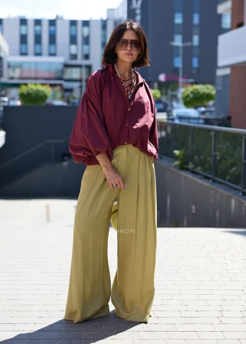 Bordowa koszula oversize z bufiastymi rękawami, zestawiona z oliwkowymi szerokimi spodniami i jasną kopertówką w eleganckiej stylizacji