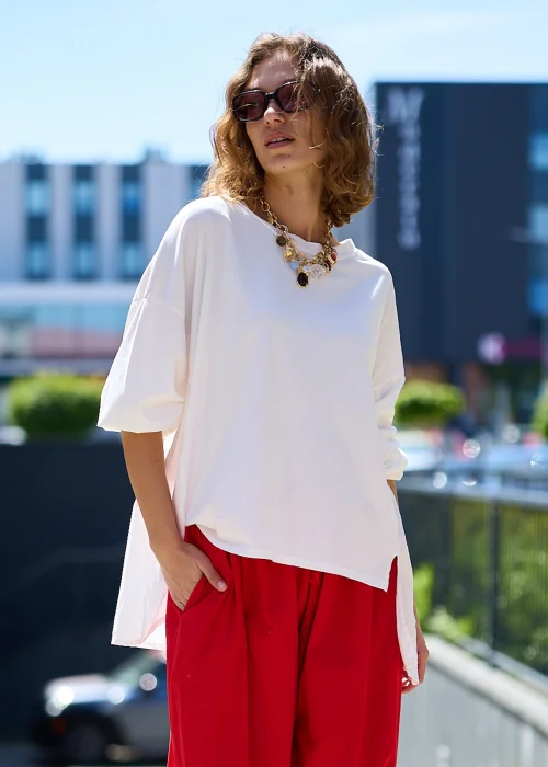 Biała bluzka oversize damska z asymetrycznym dołem i rękawem 3/4 w eleganckiej stylizacji z czerwonymi spodniami