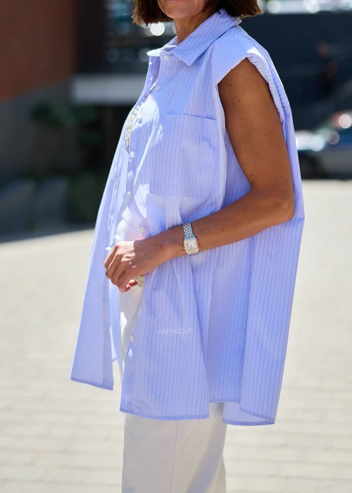 Jasnoniebieska plisowana koszula bez rękawów z kołnierzykiem i kieszenią, zestawiona z białymi spodniami w eleganckiej stylizacji