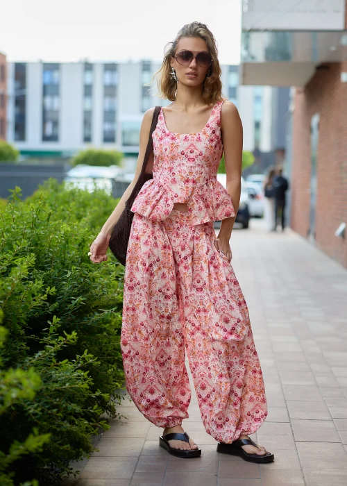 Top z szerokimi ramiączkami o dopasowanej górze i kobiecym fasonie z falbaną peplum. Model posiada szeroki, zaokrąglony dekolt oraz efektowny kwiatowo-orientalny print w odcieniach pudrowego różu, koralu
